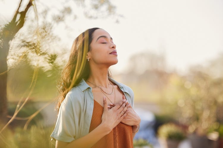 Calm woman with hands resting on her chest, practicing mindfulness outdoors.