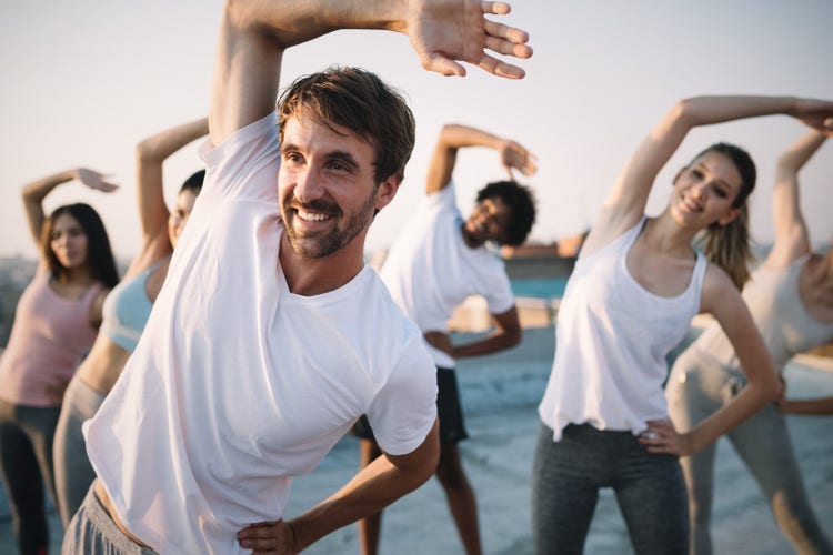 Young adults participate in a stretching exercise outdoors, highlighting the importance of movement for a healthy life.