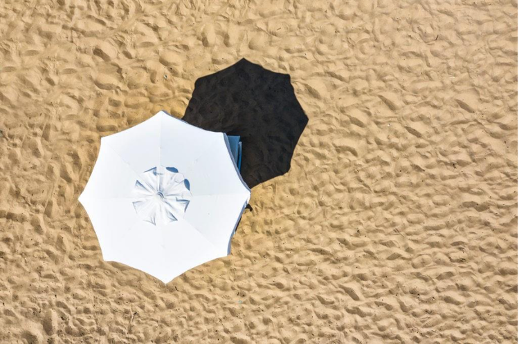White umbrella casting a shadow on a sandy beach