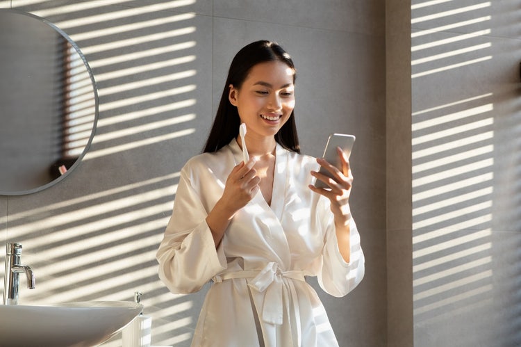 A woman holding a GUM toothbrush by Sunstar in the morning while looking at her mobile.