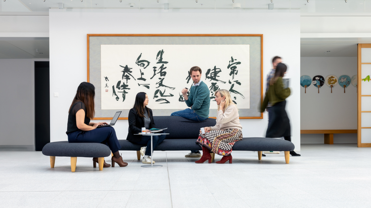 Sunstar employees sitting on a modern couch in a bright office space, having a discussion and collaborating, with Japanese calligraphy artwork in the background
