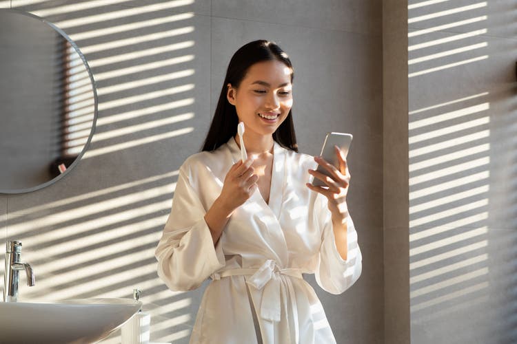 A woman holding a GUM toothbrush by Sunstar in the morning while looking at her mobile