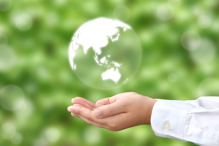 A hand gently supporting a translucent globe floating above the palm, symbolizing environmental care and sustainability, with a soft green bokeh background.